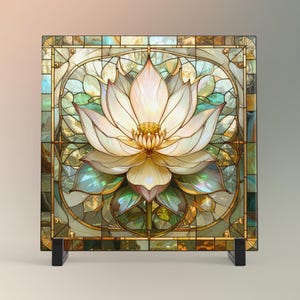 May include: A square stained glass panel featuring a white lotus flower with gold accents. The flower is centered within a frame of iridescent glass and gold lines. The panel is displayed on a black stand, creating a decorative piece.
