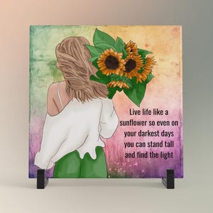 May include: A square art print featuring a woman holding sunflowers, with the text "Live life like a sunflower so even on your darkest days you can stand tall and find the light." The artwork is displayed on a black stand.