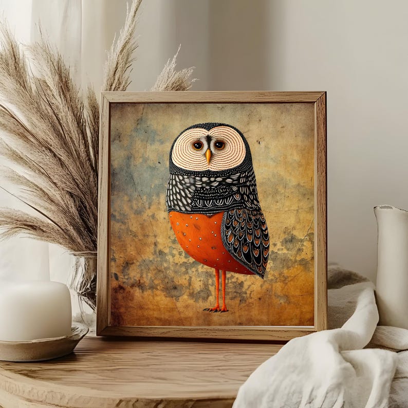 May include: Framed art print featuring a stylized owl illustration. The owl has a patterned black and white head, a vibrant orange body, and long orange legs. The artwork is set against a textured, muted background, and framed in a light wood.