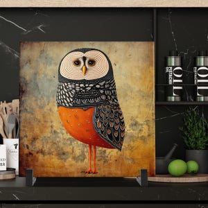May include: A square decorative panel featuring a stylized owl illustration. The owl has a cream-colored face, black and white patterned wings, and an orange body. The background is a textured, sepia-toned design.