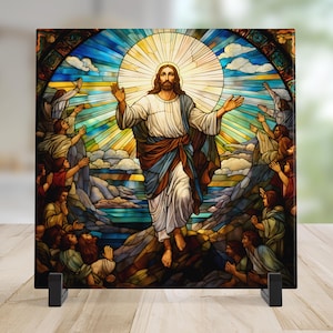 May include: A square stained glass panel depicting a religious scene. The artwork features a central figure with outstretched arms, surrounded by figures and a radiant sunburst. The color palette includes blues, yellows, and browns, creating a vibrant and detailed image.