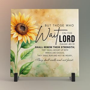 May include: A square decorative tile featuring a watercolor sunflower with yellow petals and a brown center. The tile includes the text "But those who wait on the Lord" and a Bible verse from Isaiah 40:31. The tile is displayed on a black stand.