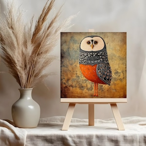 May include: An owl painting on a small wooden easel. The owl has a patterned black and white head, orange body, and long orange legs. The background is a mix of brown, blue, and yellow tones. A vase with dried plants is to the left.