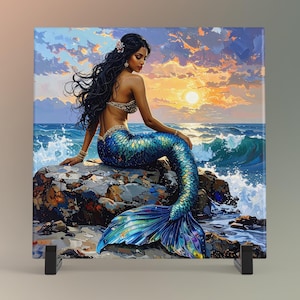 May include: A square canvas print depicts a mermaid with long black hair, a shimmering blue tail, and a seashell top, seated on a rock. The background shows a sunset over the ocean with waves and a vibrant sky.