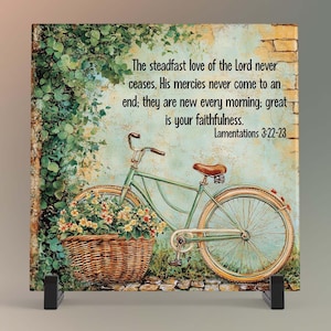 May include: A decorative square tile featuring a vintage bicycle with a basket of flowers. The bicycle is light green with brown accents. The tile includes the text "The steadfast love of the Lord never ceases..." from Lamentations 3:22-23.