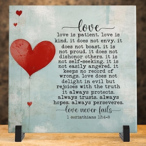 May include: A blue and white ceramic tile with a red heart and a quote about love. The quote reads "love is patient. love is kind. it does not envy. it does not boast. it is not proud. it does not dishonor others. it is not self-seeking. it is not easily angered. it keeps no record of wrongs. love does not delight in evil but rejoices with the truth it always protects. always trusts. always hopes. always perseveres. love never fails 1 corinthians 13:4-8"