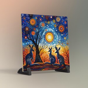 May include: A colorful ceramic tile with a blue, orange, and yellow abstract design featuring three kangaroos and a tree. The background is a starry night sky with a large yellow sun.