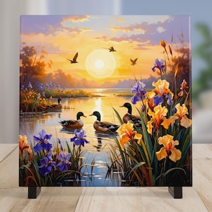 May include: A square canvas print depicting a serene lake scene at sunset. Ducks swim in the water, surrounded by colorful irises and reeds. The sky is a blend of orange, yellow, and purple hues, with birds in flight.