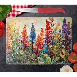 May include: A colorful glass cutting board with a watercolor painting of a field of flowers. The flowers are in shades of red, orange, yellow, blue, and purple. The background is a soft yellow with a hint of blue.