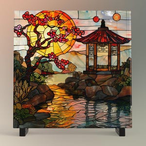 May include: A stained glass panel depicting a Japanese garden scene with a red pagoda, a cherry blossom tree, a stream, and rocks. The sun is setting behind the tree, casting a warm glow on the scene.