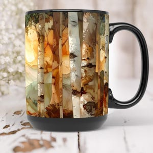 May include: A black coffee mug with a wraparound design featuring a watercolor-style forest scene. The artwork depicts birch trees in shades of brown, beige, and white, with a warm yellow and orange sunset in the background. The mug has a black handle and base.