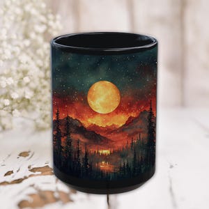 May include: Black ceramic mug featuring a vibrant landscape scene. The design showcases a large, glowing orange moon above silhouetted mountains and a forest, set against a starry night sky. The mug is a standard size.