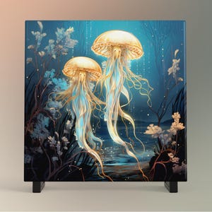 May include: Square art print featuring two glowing jellyfish with long, flowing tentacles. The jellyfish are a mix of gold and blue, set against a dark blue underwater scene with plants and a hint of light. The print is mounted on a black stand.