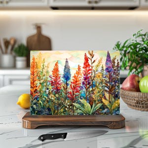 May include: A colorful glass cutting board with a watercolor painting of a field of flowers. The flowers are in shades of red, orange, yellow, blue, and purple. The cutting board is on a wooden stand.