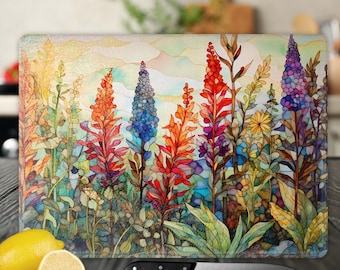 May include: A colorful glass cutting board with a watercolor-style floral design. The design features a variety of flowers in shades of red, blue, yellow, and green. The flowers are arranged in a cluster, with the tallest flowers in the center of the design. The background of the design is a light blue watercolor wash.