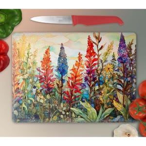 May include: A colorful glass cutting board with a watercolor painting of a field of flowers. The flowers are in shades of red, orange, yellow, blue, and purple.