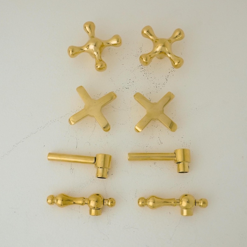 May include: Assortment of eight gold-toned cabinet knobs in various styles.  The knobs include a star shape, a cross shape, and two different styles of lever handles.