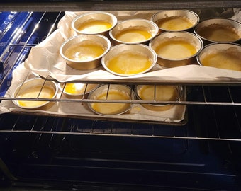 May include: A close-up of a baking sheet filled with small, round, golden-brown pies in a kitchen oven. The pies are arranged in two rows, with the top row slightly higher than the bottom row. The oven is lit and the pies are baking.