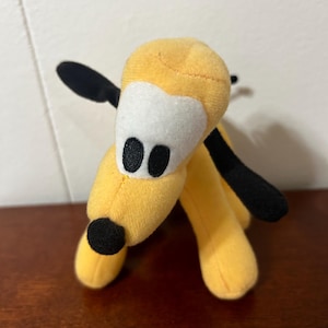 Pu&ograve; includere: Un cane di peluche giallo con orecchie e naso neri. Il cane ha occhi bianchi con pupille nere e una macchia bianca sulla fronte.