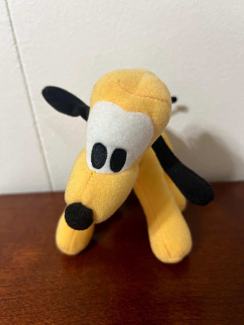 Pu&ograve; includere: Un cane di peluche giallo con orecchie e naso neri. Il cane ha occhi bianchi con pupille nere e una macchia bianca sulla fronte.