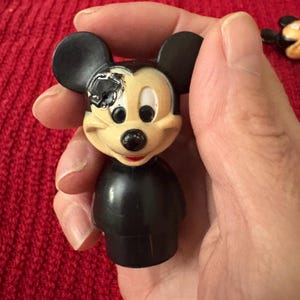 May include: A black and yellow plastic Mickey Mouse figurine with one eye missing. The figurine is wearing a black shirt and has a black nose and ears.