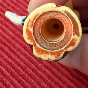 May include: Close-up of a vintage toy figure's head, featuring a yellow and brown color scheme with a small, white snake-like appendage. The base has text that reads "HONG KONG" and "WALT DISNEY PRODUCTIONS".