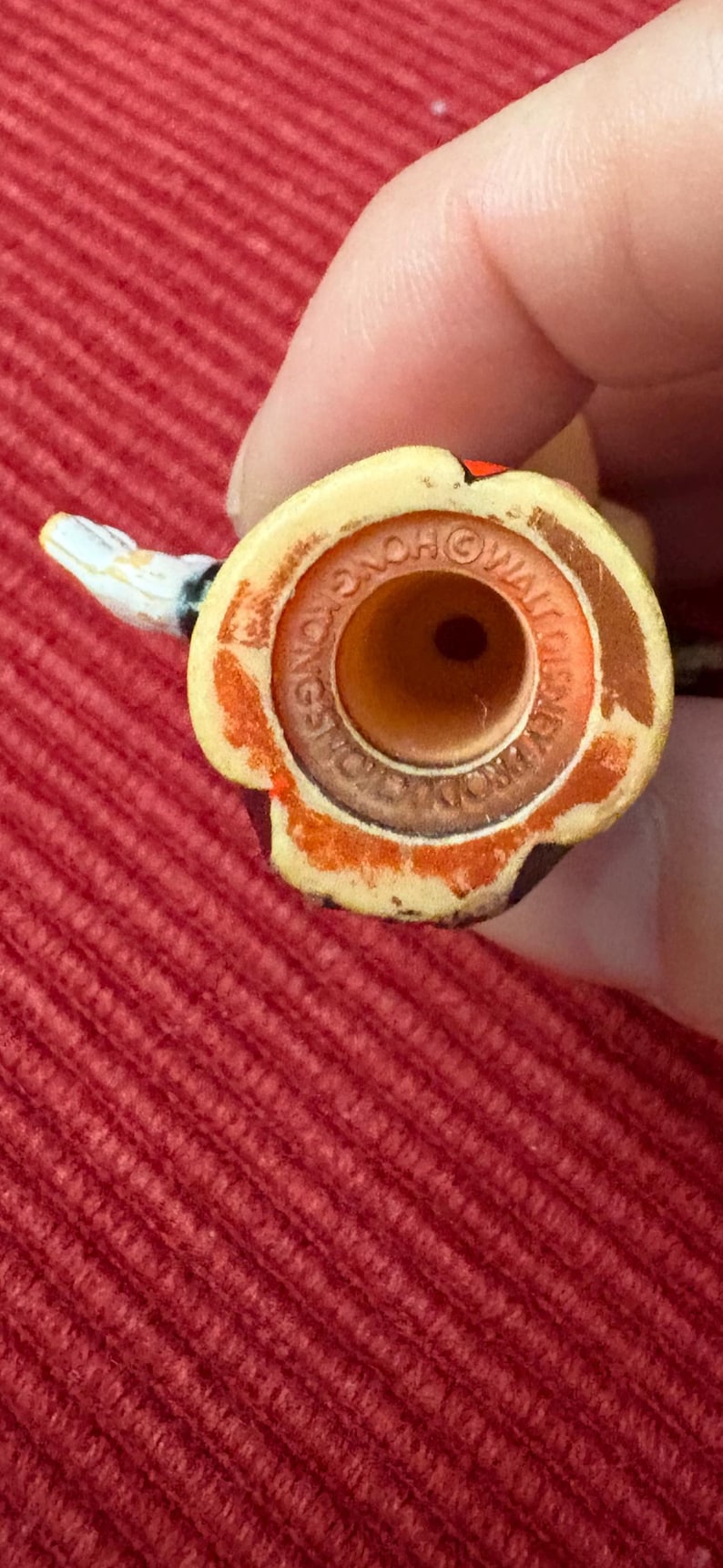 May include: Close-up of a vintage toy figure's head, featuring a yellow and brown color scheme with a small, white snake-like appendage. The base has text that reads "HONG KONG" and "WALT DISNEY PRODUCTIONS".