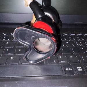 Pu&ograve; includere: Una statuetta in ceramica nera e rossa di Topolino in posizione eretta con il braccio destro alzato. La statuetta &egrave; su una tastiera di un computer portatile nero.