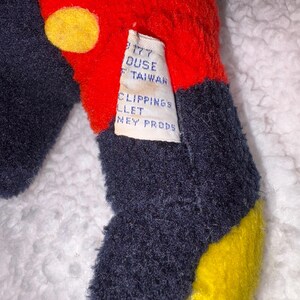 May include: Close-up of a plush toy with red, navy blue, and yellow sections. The red section has yellow circles. A tag reads "177 Duse Taiwan, Clippings Ballet, Disney Props."