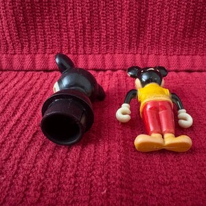 May include: Two vintage plastic Mickey Mouse figurines. One is black with a hat and the other is red, yellow, and black with a yellow shirt and red shorts.