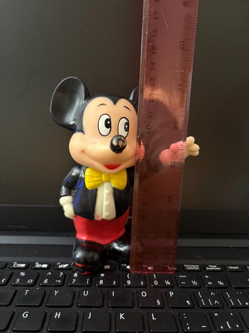 Pu&ograve; includere: Una statuetta vintage di Topolino con uno smoking nero, un papillon giallo e pantaloni rossi. La statuetta &egrave; alta circa 17 cm ed &egrave; realizzata in plastica.