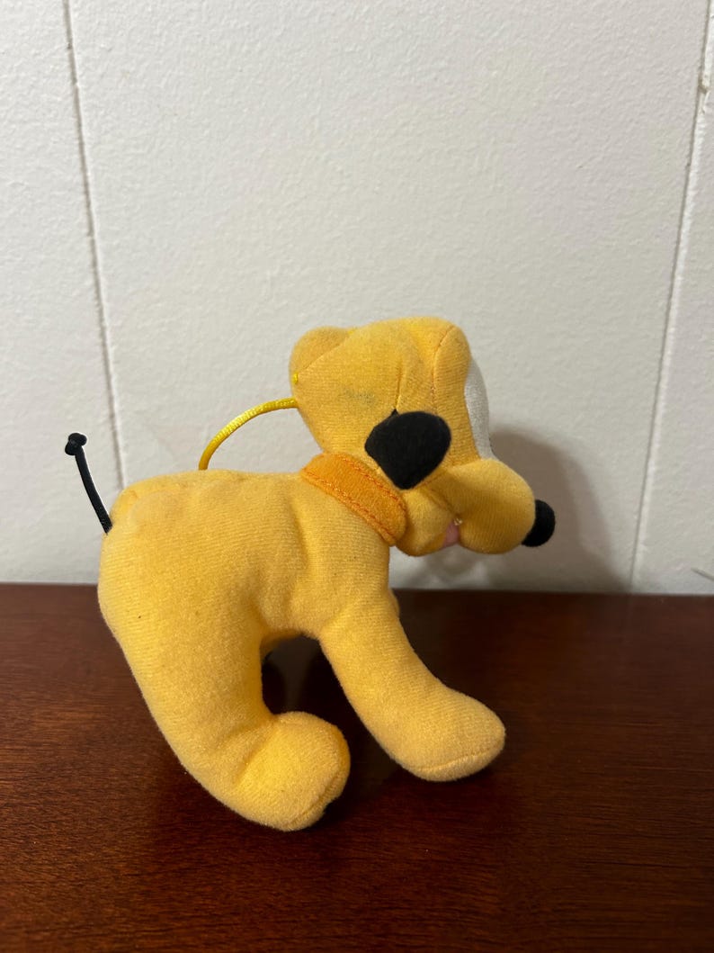 Pu&ograve; includere: Un cane di peluche giallo con orecchie nere e naso nero. Il cane indossa un collare giallo.
