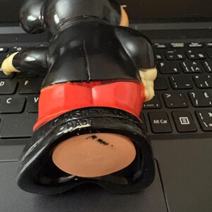May include: Black and red plastic Mickey Mouse figurine with a black base. The figurine is wearing a black suit and red shorts. The base has the text "MADE IN HONG KONG" on it.