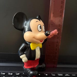 Pu&ograve; includere: Una statuetta di Topolino in gomma nera e rossa che indossa uno smoking nero con un papillon giallo. La statuetta &egrave; alta circa 18 pollici.