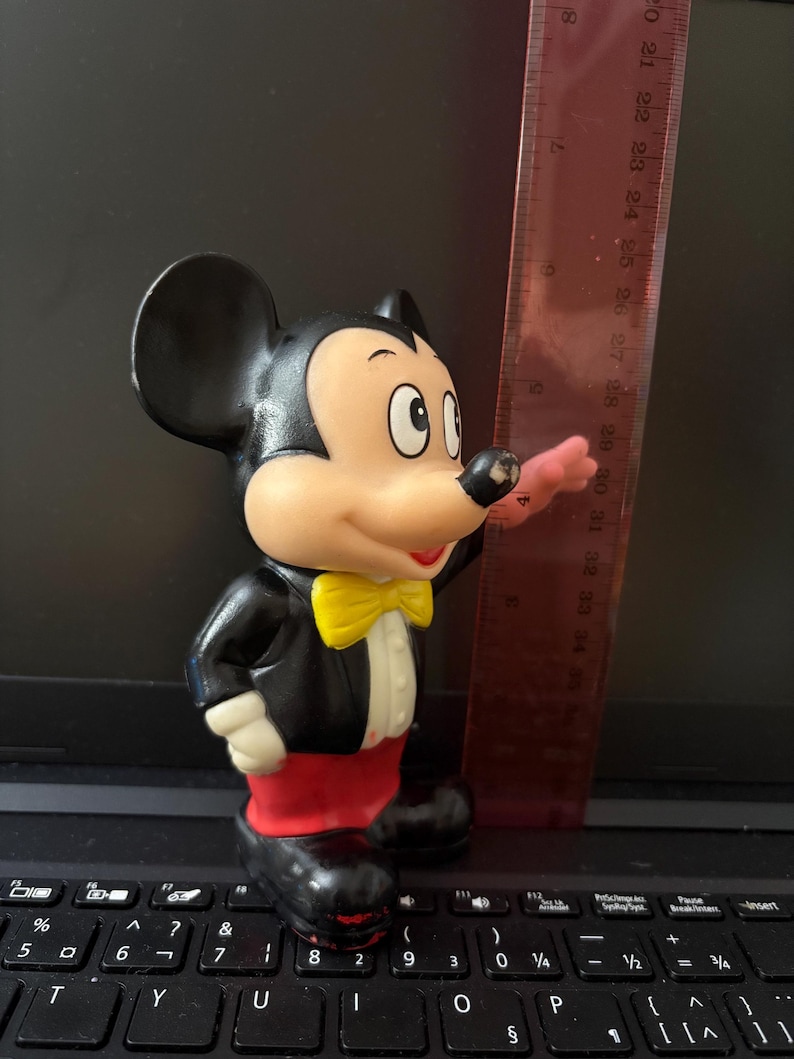Pu&ograve; includere: Una statuetta di Topolino in gomma nera e rossa che indossa uno smoking nero con un papillon giallo. La statuetta &egrave; alta circa 18 pollici.