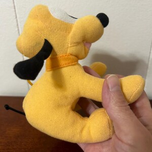 Pu&ograve; includere: Un cane di peluche giallo con orecchie nere e coda nera. Il cane ha una macchia bianca sul viso e indossa un collare arancione.