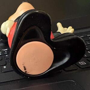May include: A black and red plastic Mickey Mouse figurine with a black base. The figurine is sitting on a black laptop keyboard.