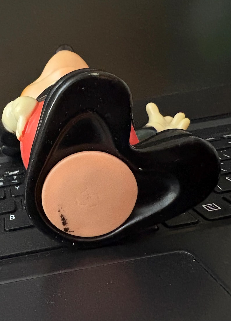 May include: A black and red plastic Mickey Mouse figurine with a black base. The figurine is sitting on a black laptop keyboard.