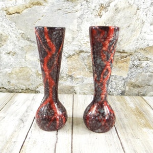 May include: Two tall, slender vases with a bulbous base and flared top. The vases have a dark brown background with a red, wavy pattern and speckled gray accents. The vases are made of ceramic and are suitable for displaying flowers.