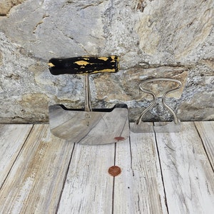 May include: Two vintage kitchen tools with black and yellow wooden handles. The first tool is a curved, stainless steel chopping knife with a black and yellow wooden handle. The second tool is a stainless steel clamp with a black and yellow wooden handle.