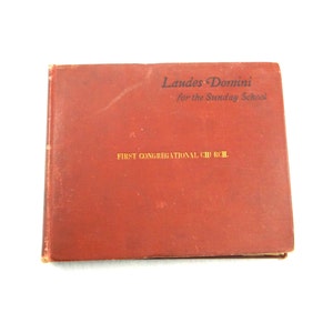 May include: A vintage, reddish-brown book titled "Laudes Domini for the Sunday School" with gold lettering. The cover also features the text "FIRST CONGREGATIONAL CHURCH."