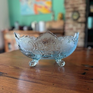 May include: A light blue glass bowl with a scalloped edge and intricate floral pattern. The bowl sits on three small feet.