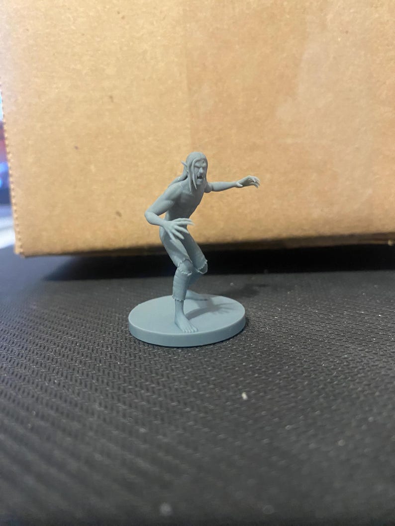 May include: A gray plastic miniature figurine of a humanoid creature with pointed ears, a snarling expression, and clawed hands. The figurine is standing on a round base.