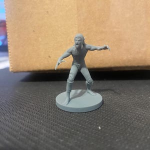 May include: A gray plastic miniature figure of a humanoid creature with pointed ears, a snarling expression, and a tattered loincloth. The figure is posed in a menacing stance with its arms outstretched and claws extended.