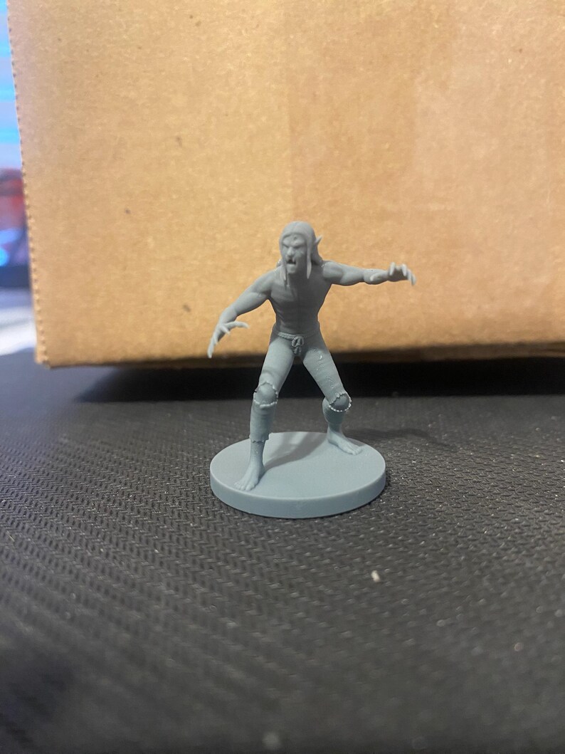 May include: A gray plastic miniature figure of a humanoid creature with pointed ears, a snarling expression, and a tattered loincloth. The figure is posed in a menacing stance with its arms outstretched and claws extended.
