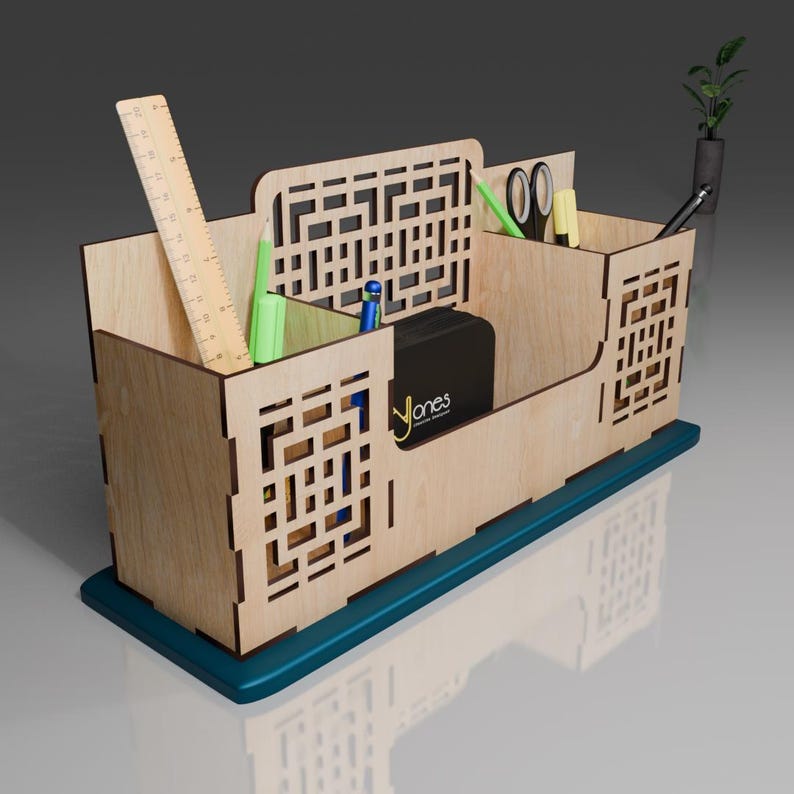 Puede incluir: Organizador de escritorio de madera con cuatro compartimentos, una regla, bol&iacute;grafos, l&aacute;pices, tijeras y una peque&ntilde;a caja negra. El organizador tiene una base azul verdosa y un patr&oacute;n geom&eacute;trico en la parte delantera.