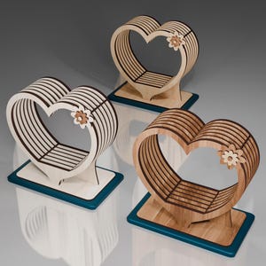 May include: Three wooden heart-shaped decorative stands with a flower design. The stands are made of light wood and have a dark wood trim. The stands are on a blue surface.