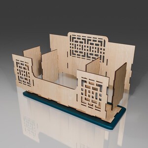 Puede incluir: Un organizador de madera con un dise&ntilde;o de corte de patr&oacute;n geom&eacute;trico. El organizador tiene una base azul verdosa y se ensambla con varias piezas.