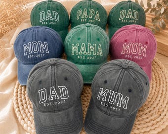 May include: A collection of nine baseball caps in various colors including green, blue, gray, and pink. Each cap features embroidered white lettering with titles such as DAD, PAPA, MOM, MAMA, or MUM, accompanied by an established year like EST. 2026 or 2027.