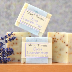 Puede incluir: Tres barras de jabón de lavanda hecho a mano con flores de lavanda secas. El jabón está etiquetado como "Island Thyme Orcas Lavender Soap Artisan Soaps from the San Juan Islands."